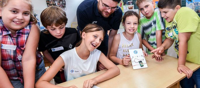 Eine Gruppe von Kindern und ein Erwachsener in einem Klassenzimmer, die TUEV Kids Strom Bausätze zusammenbauen.
