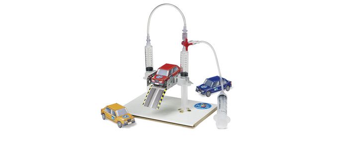 Ein Laboraufbau mit drei Miniaturautos, die an Schläuchen befestigt und mit einem zentralen Gerät verbunden sind, das auf einer weißen Plattform mit einem blauen, runden Emblem steht.
