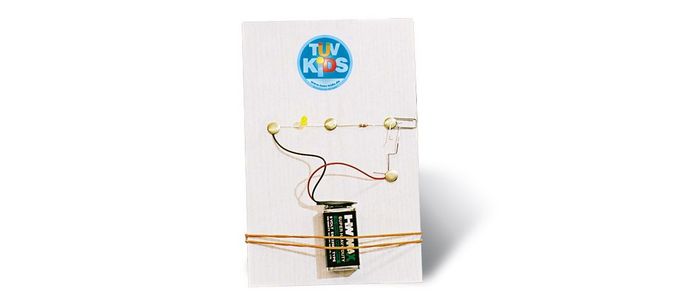 Eine Produktverpackung mit einem blauen Logo mit der Aufschrift "TUEV Kids", einem rechteckigen elektronischen Bauteil und einer Reihe von daran befestigten Drähten.