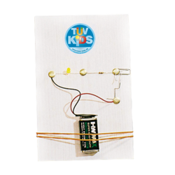 Eine einfache elektrische Platine mit einer Batterie, Drähten und einer Glühbirne, beschriftet mit "TUEV KIDS".