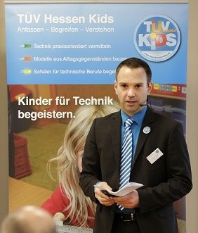 Steffen Seehars steht vor einem Banner, das für ein Programm namens "TÜV Kids" wirbt.