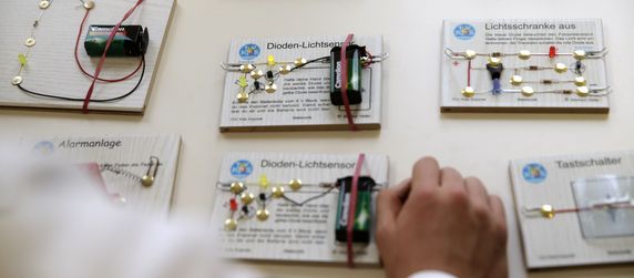 Verschiedene elektronische Schaltkreise, die jeweils mit ihrem Namen und einer kurzen Beschreibung versehen sind, zusammen mit einer Batterie und Anschlusskabeln.